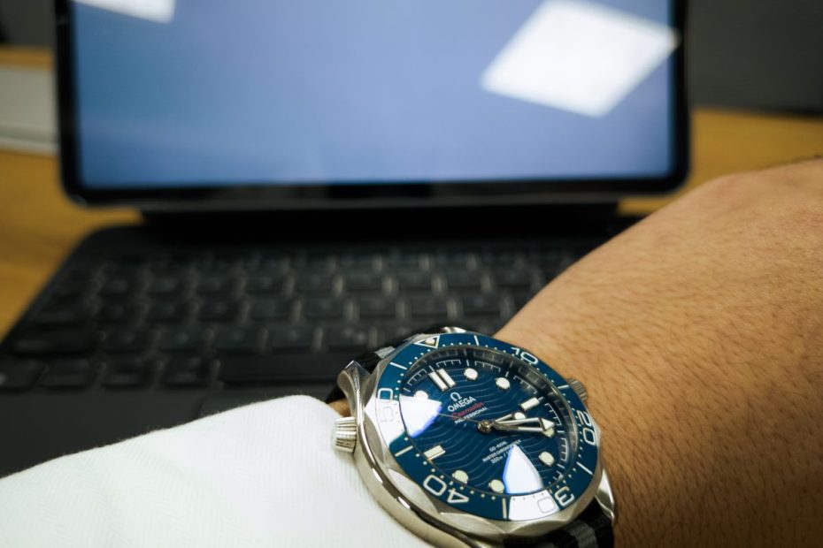 Omega Seamaster watch on a wrist in front of an iPad showing a propeller aircraft